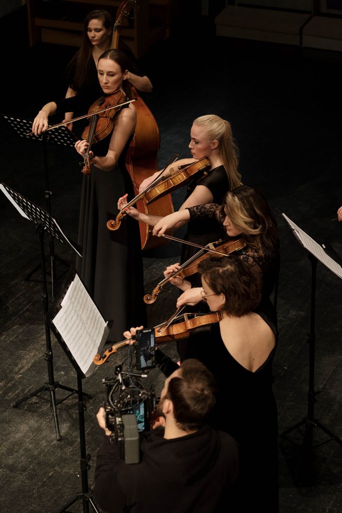 Orchestra musicians in elegant black dresses play string instruments on stage.